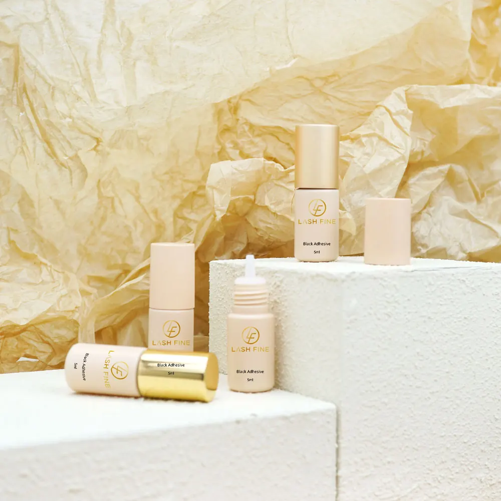 Lash Fine black lash adhesive bottles staged on white plinths with gold paper