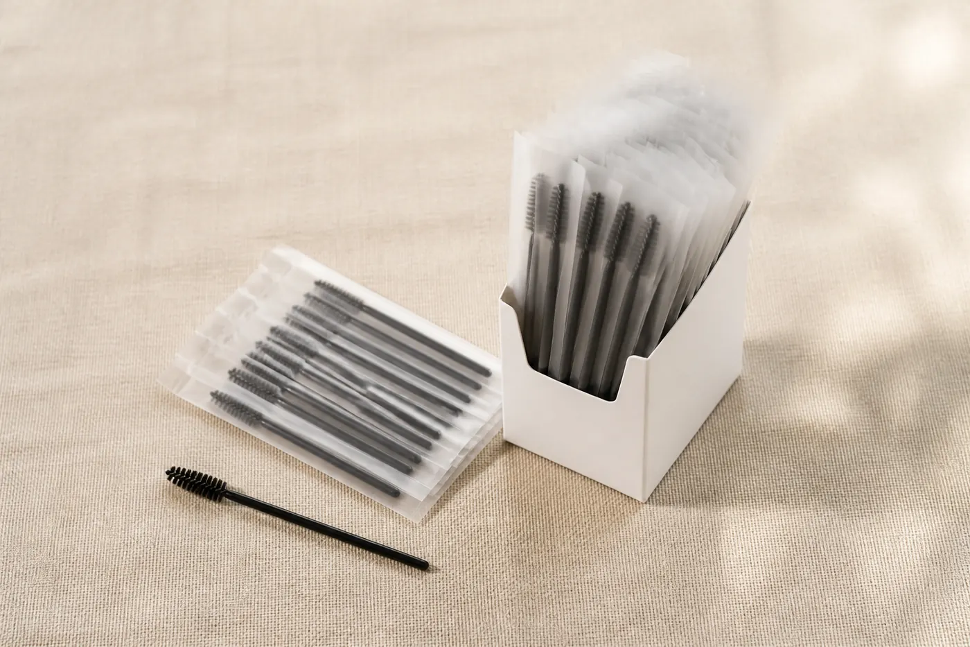 Lash brushes packed in clear sleeves beside a plain white dispenser box