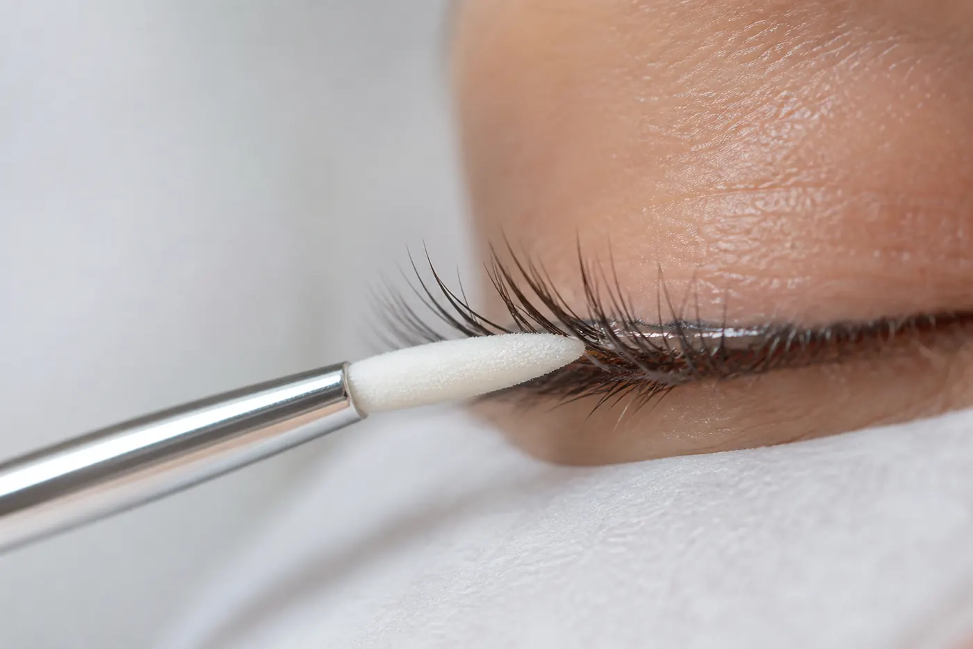 Macro photograph of a micro brush applying primer along a closed eye's lash line