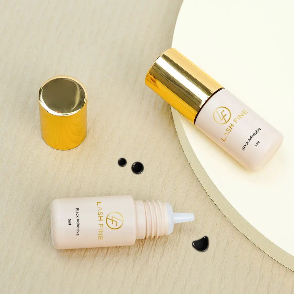 Lash Fine black adhesive bottles with the cap removed and adhesive drops beside them